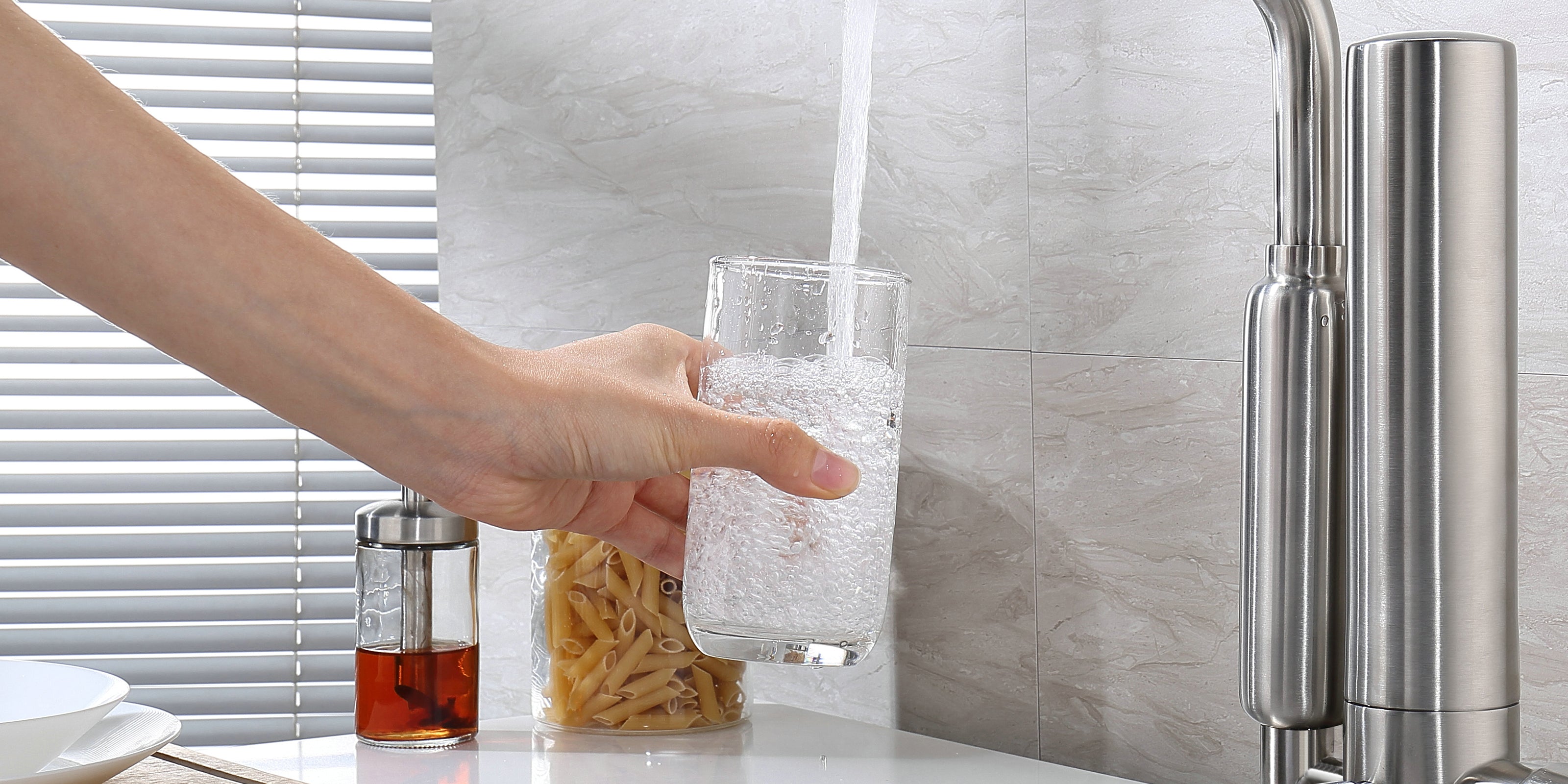 Person filling a glass with water from a kitchen faucet.